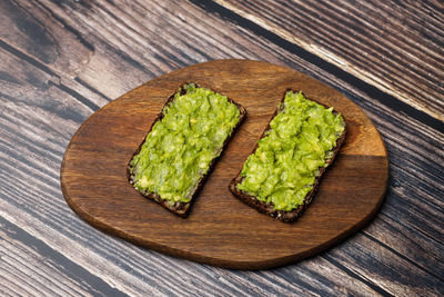 Guacamole and avocado paste are spread on dark rye bread. delicious avocado toast on cutting board. 