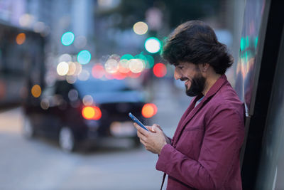 Young man with smartphone at night time with city view  in the background. mobile, technology, urban 