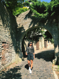 Woman in gray long-sleeve t-shirt and black shorts walking on a paved path on a castle