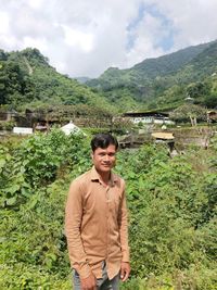 Portrait of young man standing by plants against mountains and sky