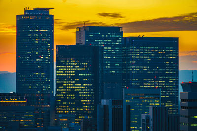 Illuminated modern buildings in city against sky at night