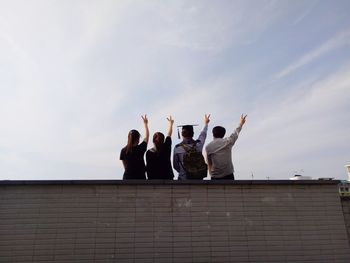 Rear view of friends gesturing peace sign on roof against sky