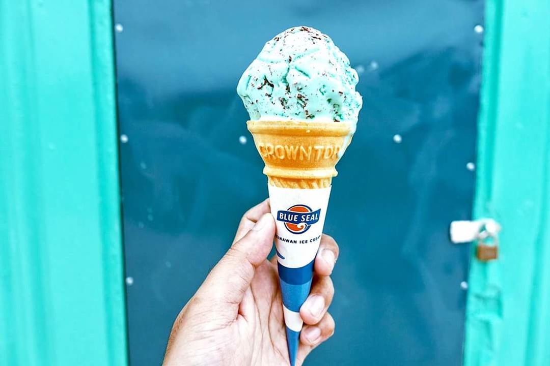 HAND HOLDING ICE CREAM CONE AGAINST BLUE GLASS