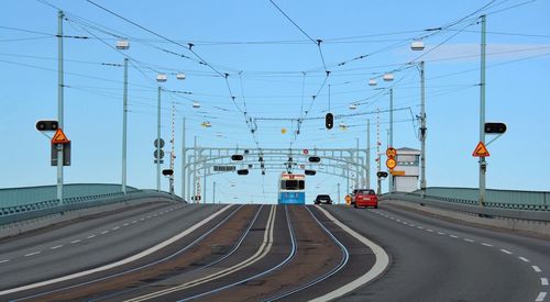 Road by electricity pylons against clear sky