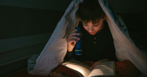 Boy reading book in darkroom at home