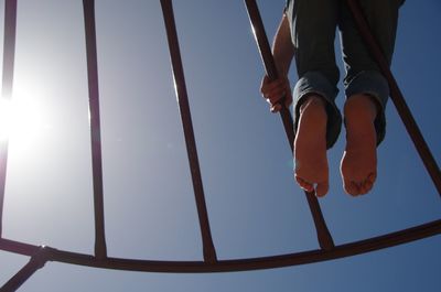 Low section of man standing on swing against sky