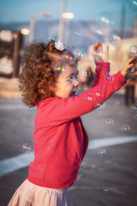 Side view of happy girl playing bubbles on road 