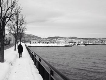 Rear view of silhouette man walking on snowcapped bridge during winter