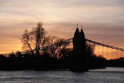 Silhouette of bridge over river against cloudy sky