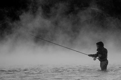 Side view of man fishing in sea during foggy weather