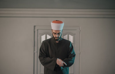 Young man looking away while standing against wall