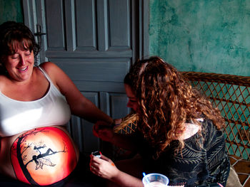 Friend making painting on pregnant woman stomach at home