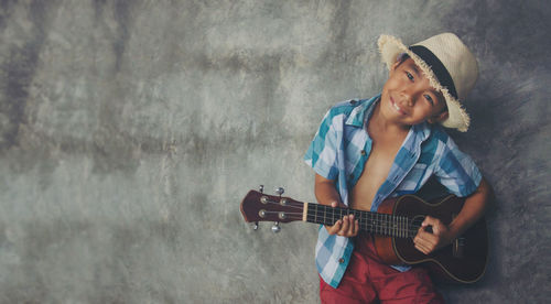 Boy playing guitar against wall