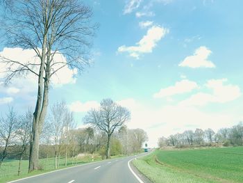 Road by trees on field against sky