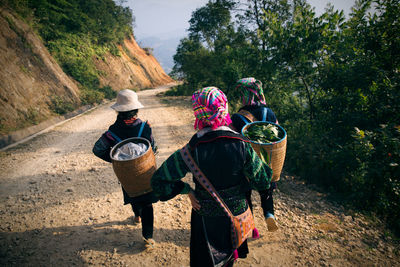 Rear view of women carrying baskets while walking on dirt road