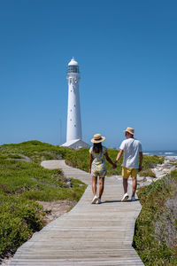 Rear view of woman standing on boardwalk against clear blue sky