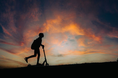 Silhouette man walking on field against orange sky during sunset