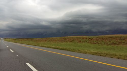 Empty road amidst field against sky