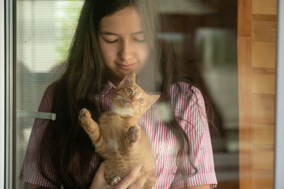 Girl with kitten staying near the window