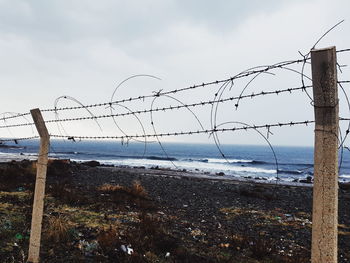 Barbed wire fence on beach against sky