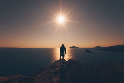 Silhouette man standing at sea shore against sky during sunset