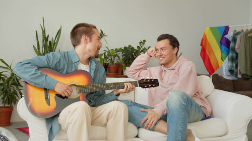 Man playing guitar while sitting with friend at home