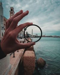 Cropped image of hand holding bangle against building by sea