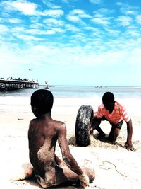 Men sitting on beach against sky