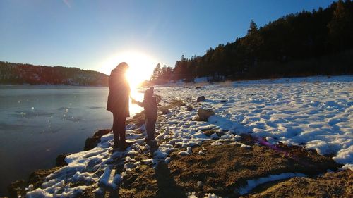 Woman standing by frozen lake against sky during sunset