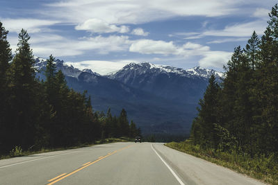 Empty road along trees and mountains against sky