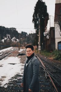 Portrait of young man standing on railroad tracks during winter