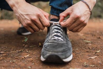 Crop faceless male hiker tying laces of gray sneakers during trekking in woods