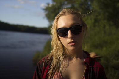 Portrait of woman wearing sunglasses against lake on sunny day