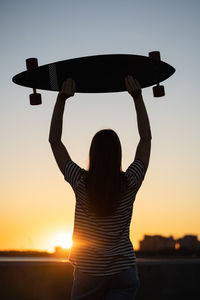 Freedom and urban lifestyle teenage skater girl with longboard look at sunset back view