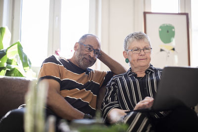 Woman using laptop while man sitting by on sofa