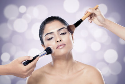 Cropped hands of people applying make-up on woman face against colored background