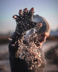 Close-up of man throwing sand at beach against sky