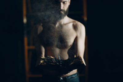 Midsection of shirtless woman standing against black background