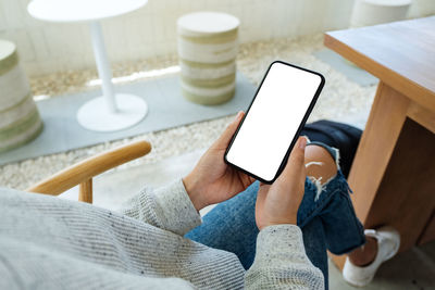 Mockup image of a woman holding mobile phone with blank white desktop screen