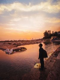 Young man looking up while standing on staircase by lake during sunset