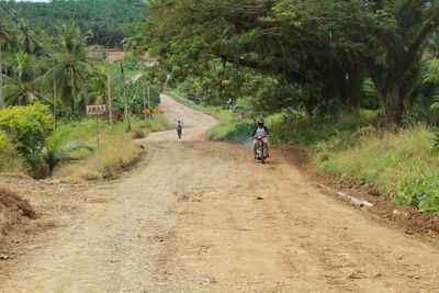 Rear view of man riding motorcycle on dirt road