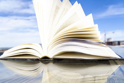 Close-up of open book on table against sky