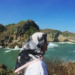 Side view of young woman in hijab standing by river against clear blue sky