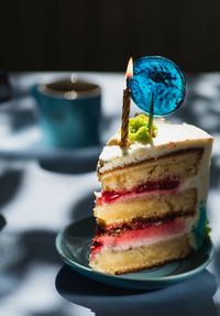 Plate with slice of tasty homemade raspberry cake. colorful lollipop swirl on stick. burning candle