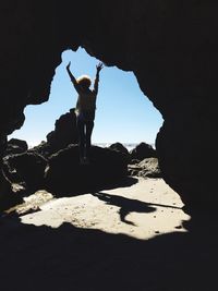 Rear view of woman jumping at beach seen through cave