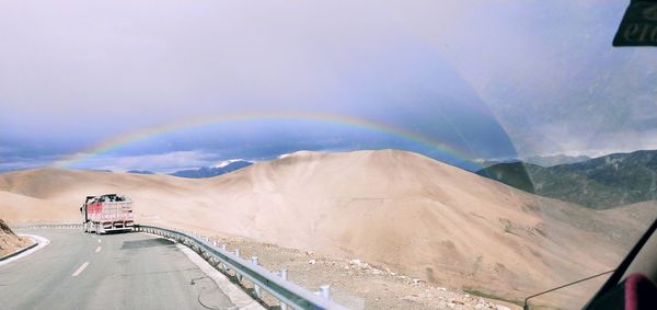 Scenic view of road against rainbow in sky