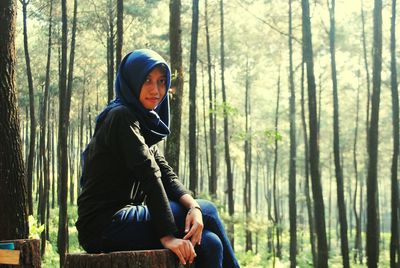 Portrait of woman in hijab sitting on tree stump in forest