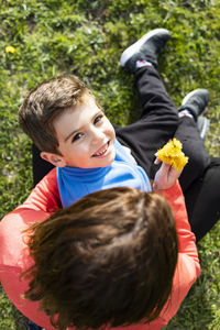 Portrait of boy with mother holding yellow flowers while sitting on land