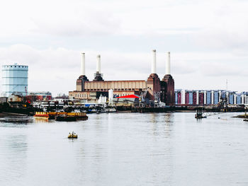 Boats in river by buildings in city against sky