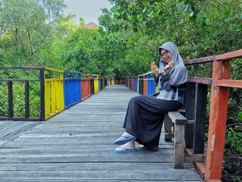 Side view of man sitting on railing against trees